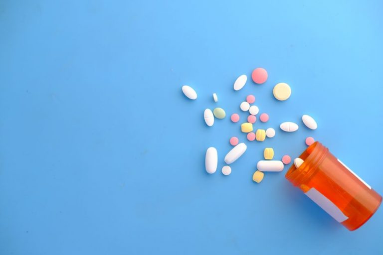 An assortment of colorful pills scattered from a prescription bottle on a blue background.