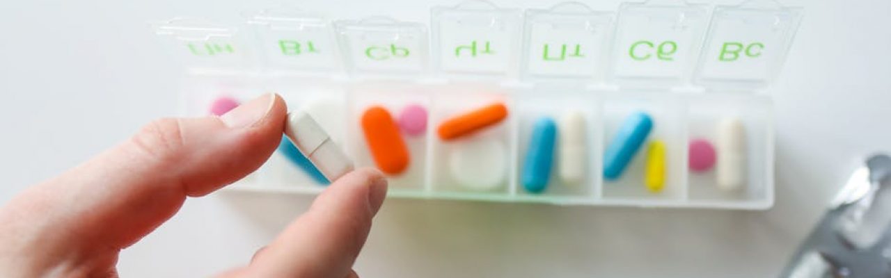 Close-up of a hand selecting a pill from a weekly pill organizer, illustrating daily health and medication routines.