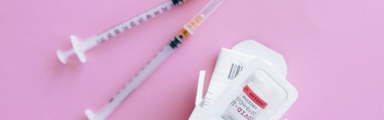 Close-up of vaccine vial and syringes on a pink background, representing healthcare.