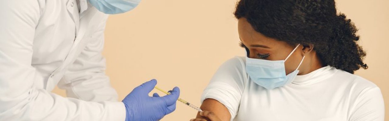 A medical professional giving a vaccine injection to a patient wearing face masks for safety.