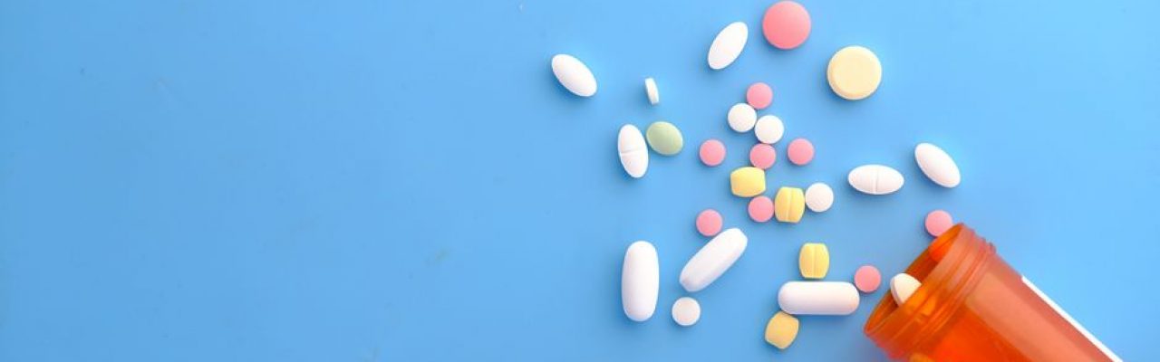 An assortment of colorful pills scattered from a prescription bottle on a blue background.